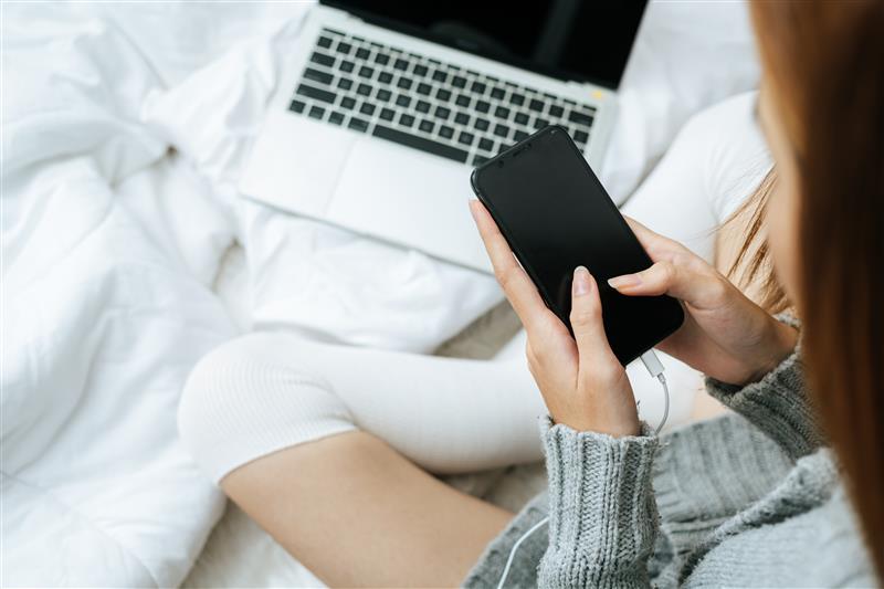 content creator sitting on bed turnign phone and laptop on to start organizing video content.jpg